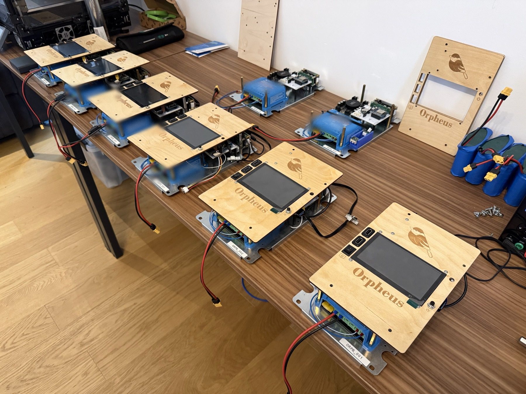 A build batch of Orpheus units on the workbench — laser-engraved faceplates, charge controllers, and battery packs mid-assembly